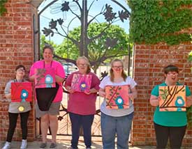 A group of young women showing off their paintings in an outdoor setting. Part of a program through Fine Arts Institute of Edmond.